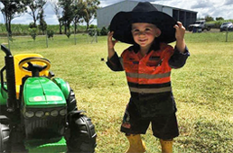 Child with hat next to tractor on peanut farm